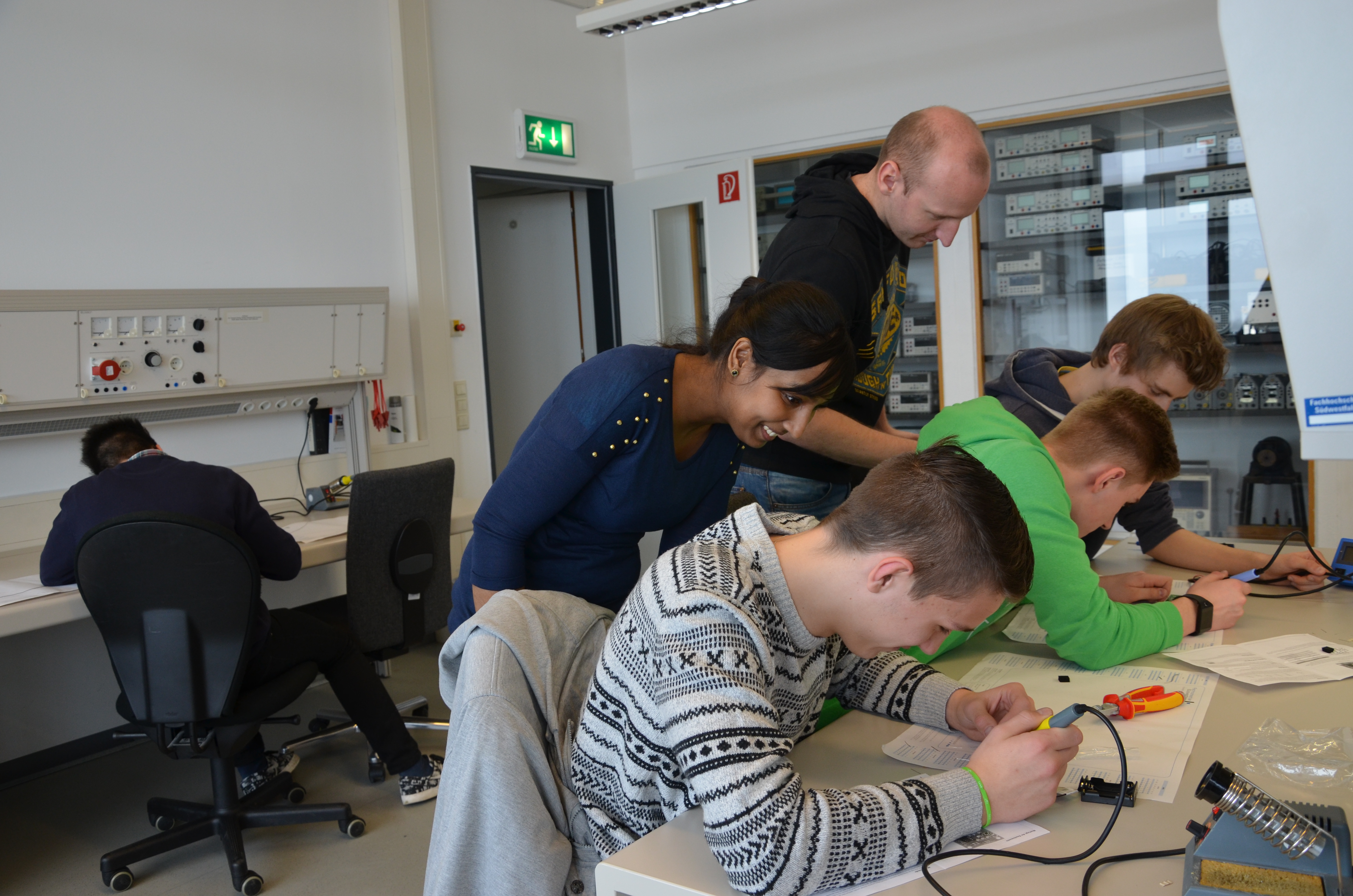 Tharsika Sivalingam vom zdi und FH-Mitarbeiter Tim Kortmann schauen den Schülern der Gesamtschule Haspe bei ihrer Löt-Arbeit über die Schultern. 