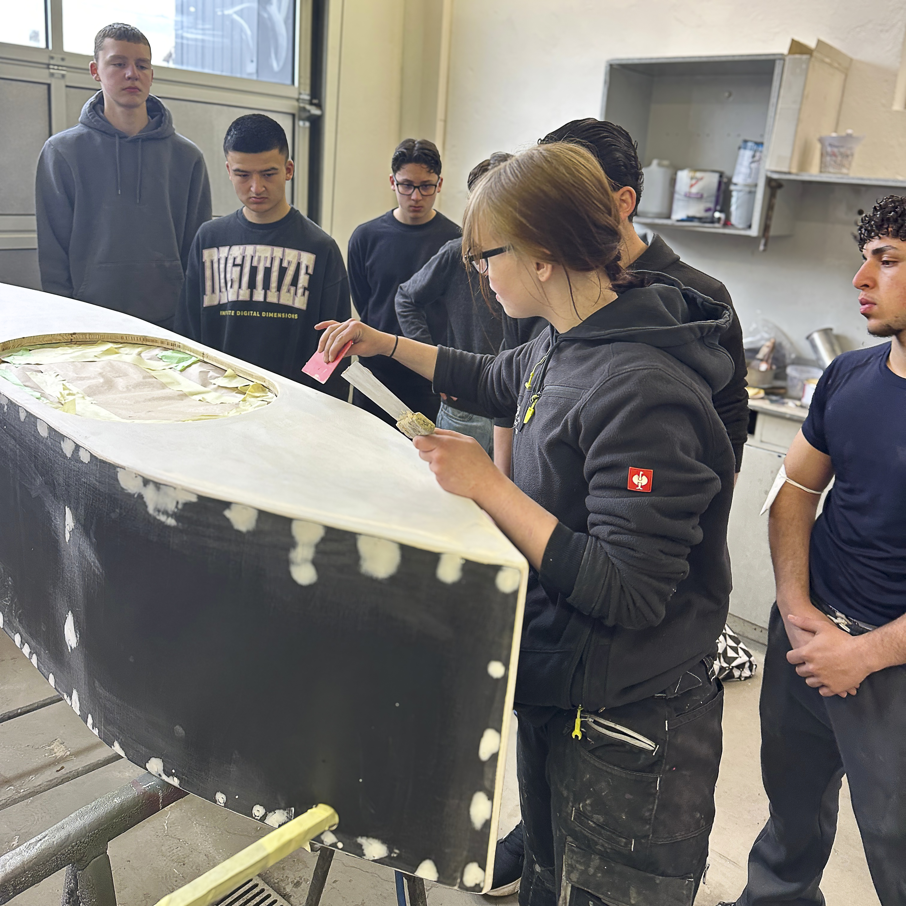 Die Auszubildende Celine im Lackier- und Karosseriezentrum Bremer bereitet mit den Jugendlichen eine Seifenkiste zur Lackierung vor / Foto: Sabrina Becker. FH Südwestfalen