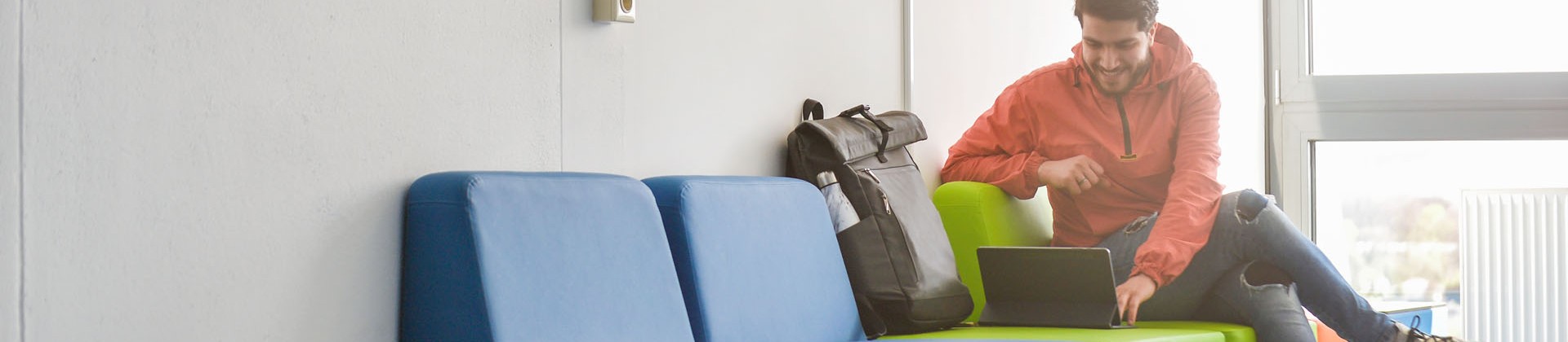 Studierender sitzt auf dem Flur der Hochschule und schaut auf ein Tablet.