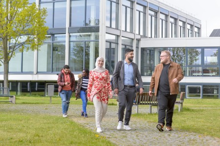 Studierende laufen in Grüppchen über den Innenhof am Hagener Standort und unterhalten sich.