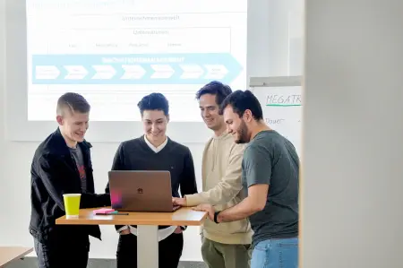 Studierende Personen mit in einem Raum mit Leinwand und einer PowerPoint mit dem Thema Inovationsmanagement