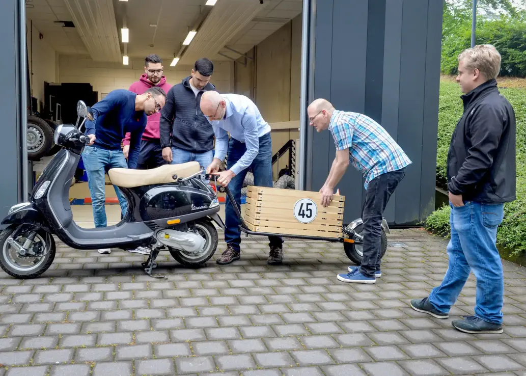 Studierende Personen die an einem Roller einen Anhänger anhängen.