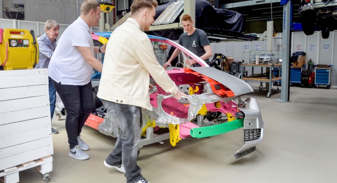 Vier Menschen schauen sich die Karosserie eines Autos an.