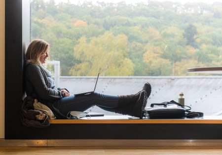 Studentin sitzt am Fenster mit einem Laptop