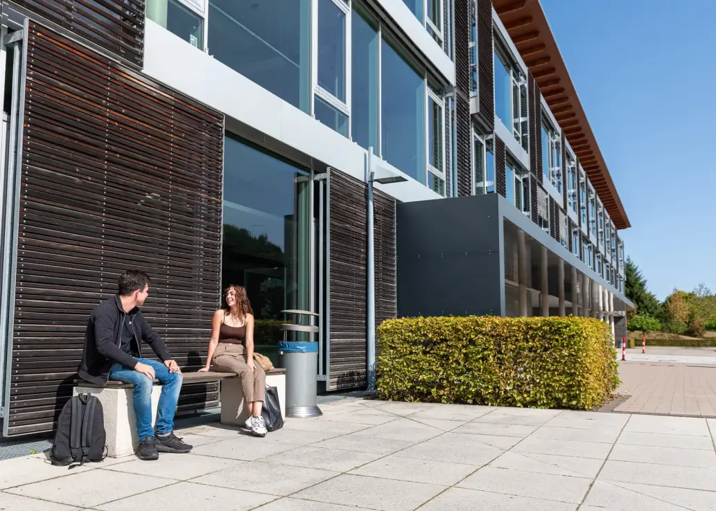 Zwei Studierende sitzen vor dem Hochschulgebäude am Standort Meschede