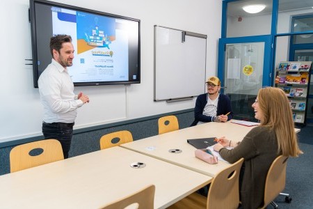 Dozent erklärt im Seminarraum zwei Studierenden eine Powerpoint-Präsentation