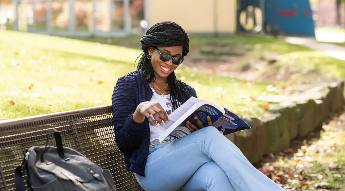Studentin am Campus Soest auf einer Bank am Buch lesen