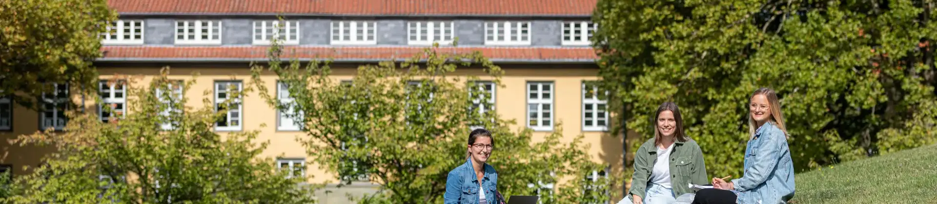 Drei Studierende sitzen auf der Wiese am Soster Campus