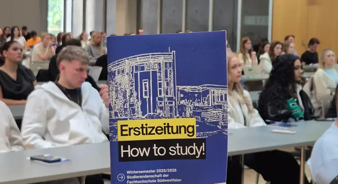 Ein Raum voller Studierender, im Vordergrund sieht man das Deckblat der Ersti-Zeitung der Studierendenschaft der Fachhochschule Südwestfalen.