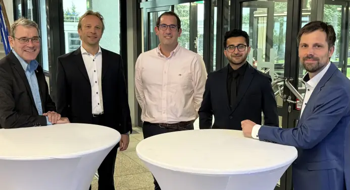 Das Bild zeigt die folgenden Herren am Sttehtisch: Henrik Ostermann (Mitte) und Zubair Javed (2. v. re.) arbeiten künftig bei Kniit zusammen. Sehr zur Freude von Prof. Dr. Andreas de Vries, Prof. Dr. Christian Leubner und Prof. Dr. Henning Femmer (v.li.). 