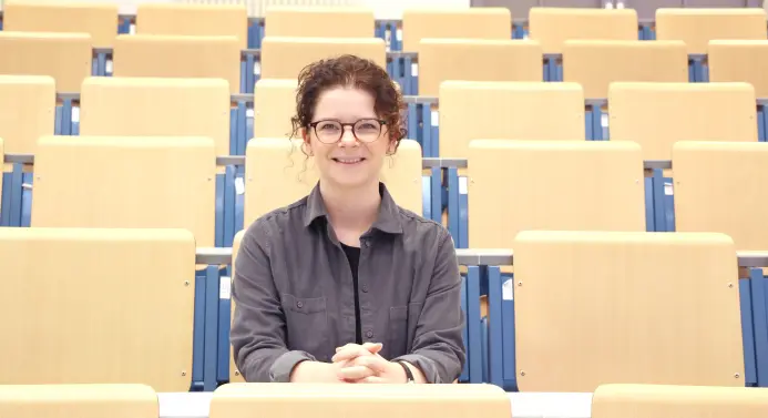 Prof. Dr. Kristina Kusanke lehnt an einem Bücherregal in einer Bibliothek.