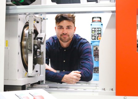 Student im Labor schaut zwischen Umformtechnik-Anlagen in die Kamera.