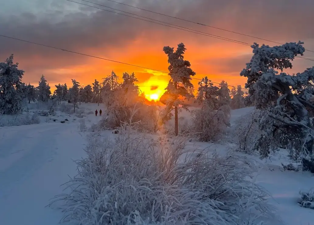 Zwei Menschen spazieren bei Sonnenuntergang in einer Schneelandschaft.