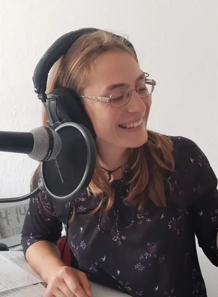 Eine Frau sitzt vor einem Mikrofon und trägt Kopfhörer.