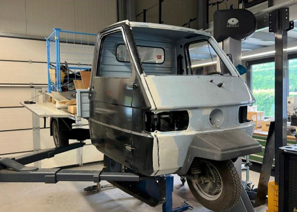 eine Ape auf einer Hebebühne von links vorne fotografiert.