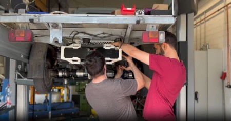 Zwei Männer arbeiten an einer Ape, die auf einer Hebebühne ist.