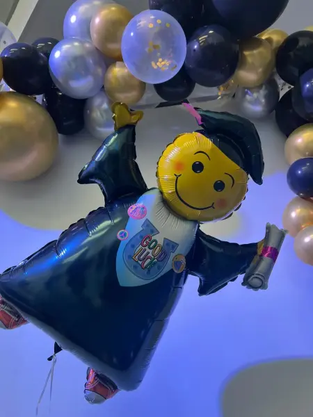 Luftballon in Form eines Männchens mit gelbem Kopf, welches eine Absolvierendenrobe und einen Abschlusshut trägt.