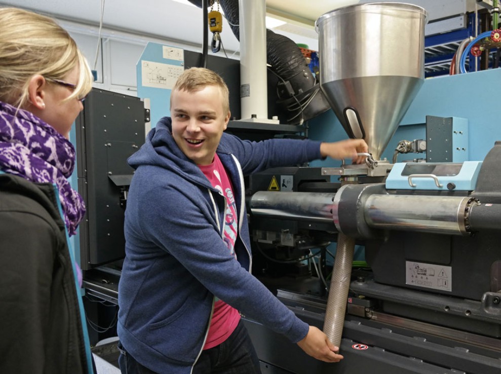 Studierender zeigt einer Frau das bedienen einer Maschine