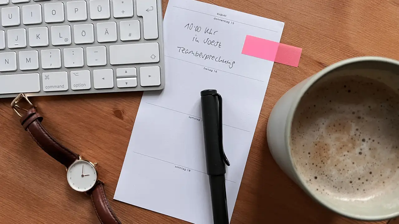 Tastatur, Uhr, Stift auf einem Zettel und eine Kaffeetasse