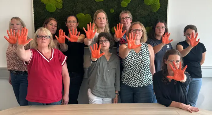 Mitarbeiterinnen der Hochschule halten die rechte Hand in die Luft, an der sie orangene Handschuhe tragen
