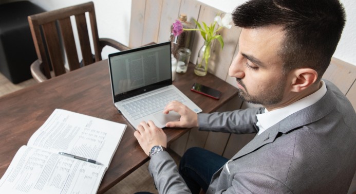 Ein Student sitzt mit Buch und Laptop am Schreibtisch